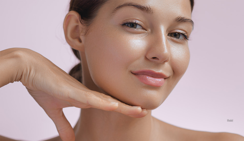 a smiling young woman feels the defined contours of her chin.