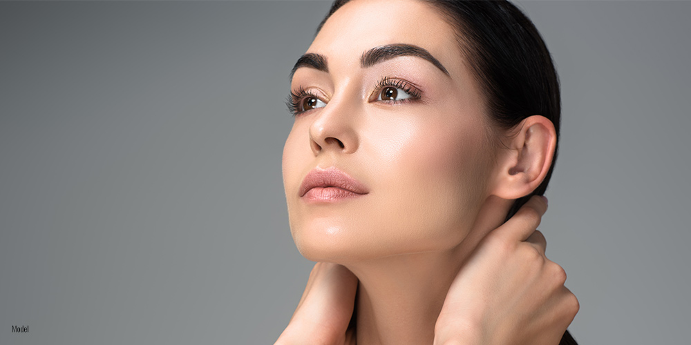 Woman looking up away from the camera with her hands on the back of her neck.